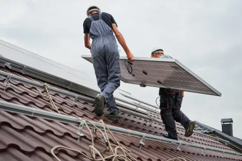 Zwei Monteure installieren ein Solar-Modul auf einem Dach.